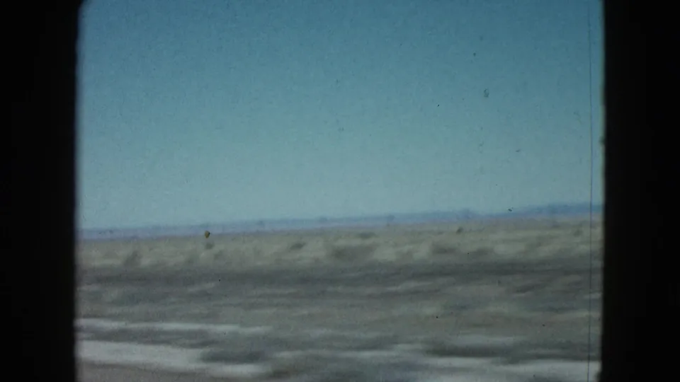 1958 8mm frame showing open Nevada desert horizon and scrubby ground filmed from a moving car window.