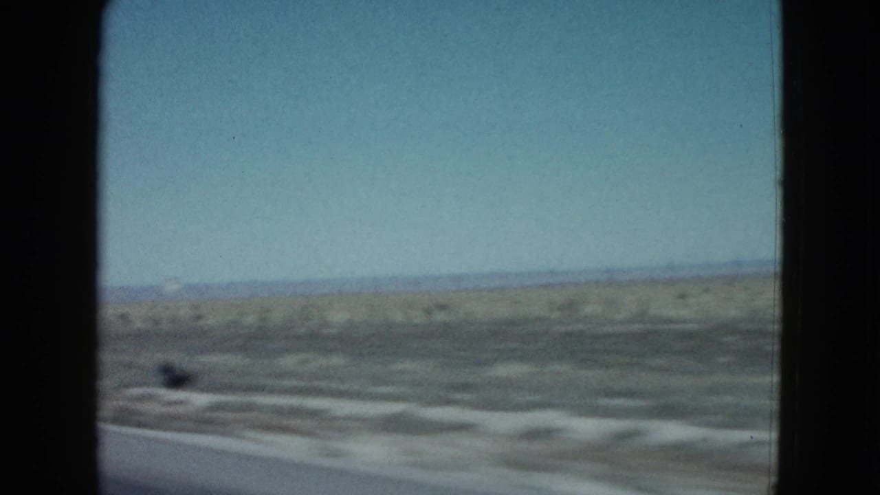 Blurred desert terrain seen through a vehicle windshield from a moving car.