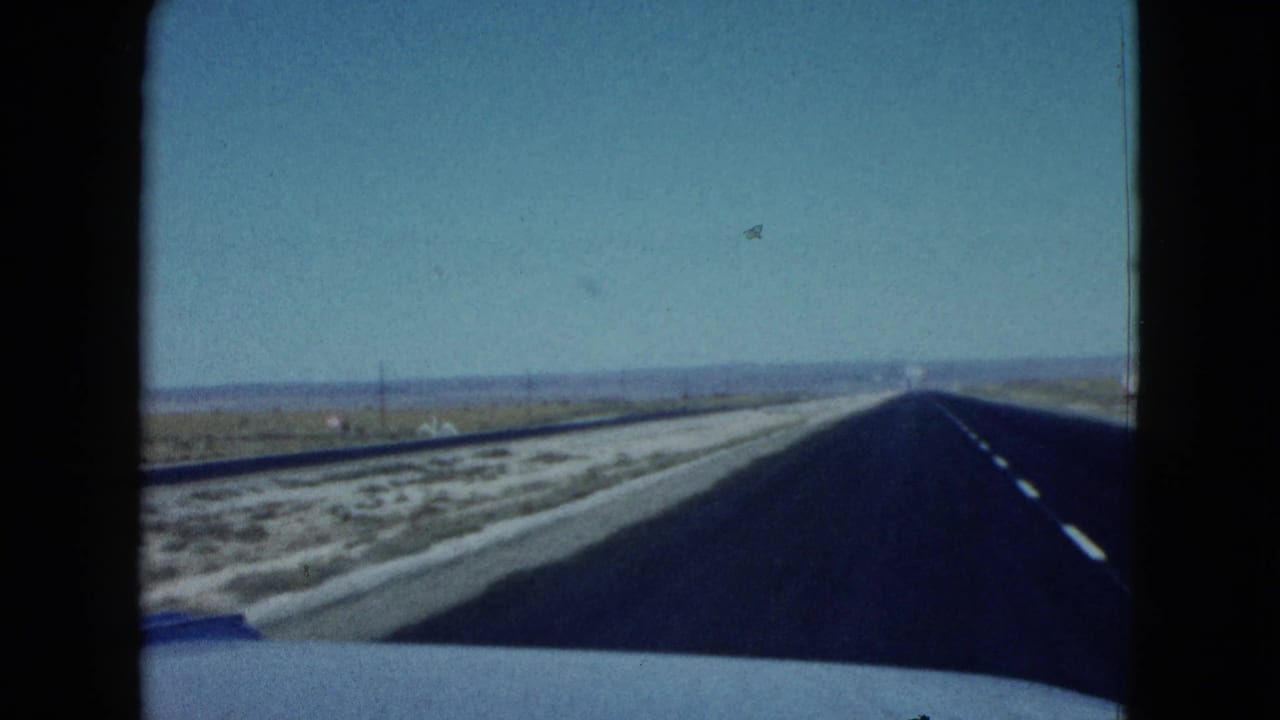 Straight desert highway seen through a car windshield with blue car trim at the bottom.