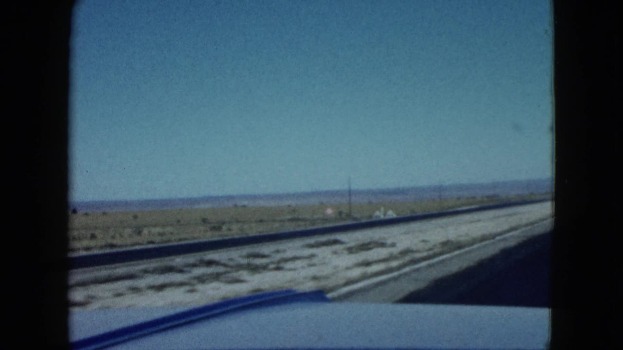 Roadside desert landscape and highway shoulder seen from inside a moving car.