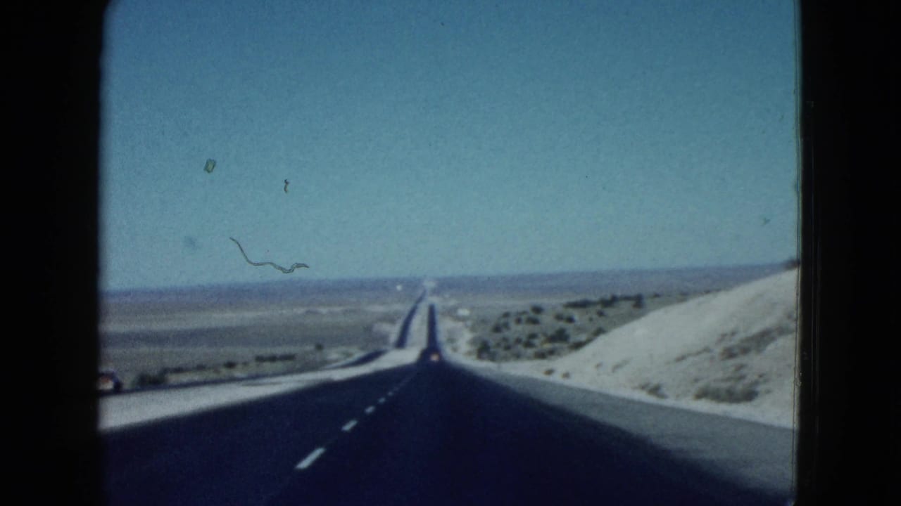 1958 8mm Las Vegas-area travel view showing a straight blacktop road through open desert with low mountains in the distance.