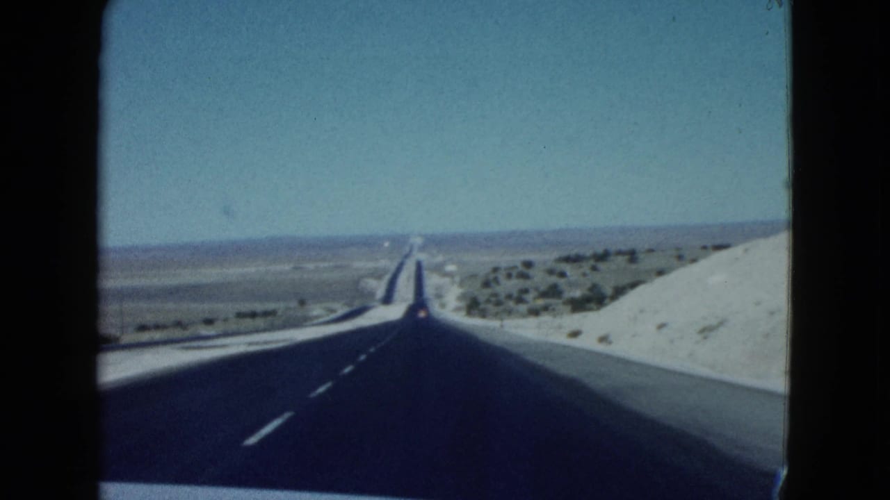 Forward-facing 1958 Nevada desert road view with blacktop pavement, pale roadside slopes, and open horizon.