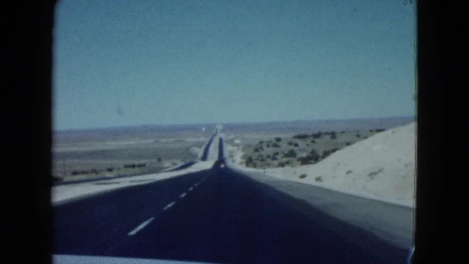 Forward-facing 1958 Nevada desert road view with blacktop pavement, pale roadside slopes, and open horizon.
