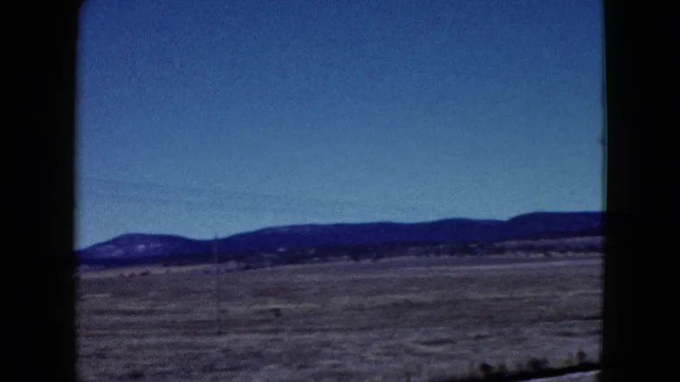 1958 Las Vegas-area desert landscape seen from a moving vehicle, with dry flats and low mountains across the horizon.