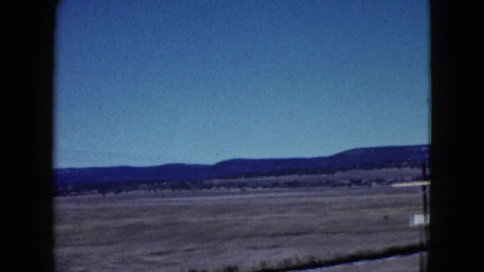 Late-1950s 8mm travel frame showing open Nevada desert, distant hills, and roadside foreground from a moving car.