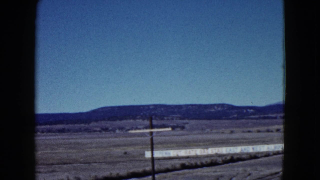Roadside desert view with a utility pole, long pale sign, low ridge, and cloudless sky.