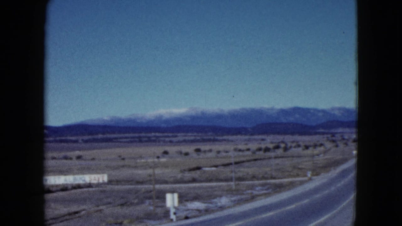 Two-lane desert highway leading toward snow-capped mountains under a blue sky.