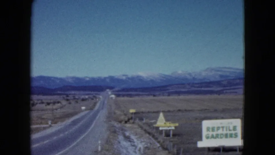 1958 Las Vegas-area 8mm frame showing a desert highway, mountains, and a readable Reptile Gardens roadside sign.