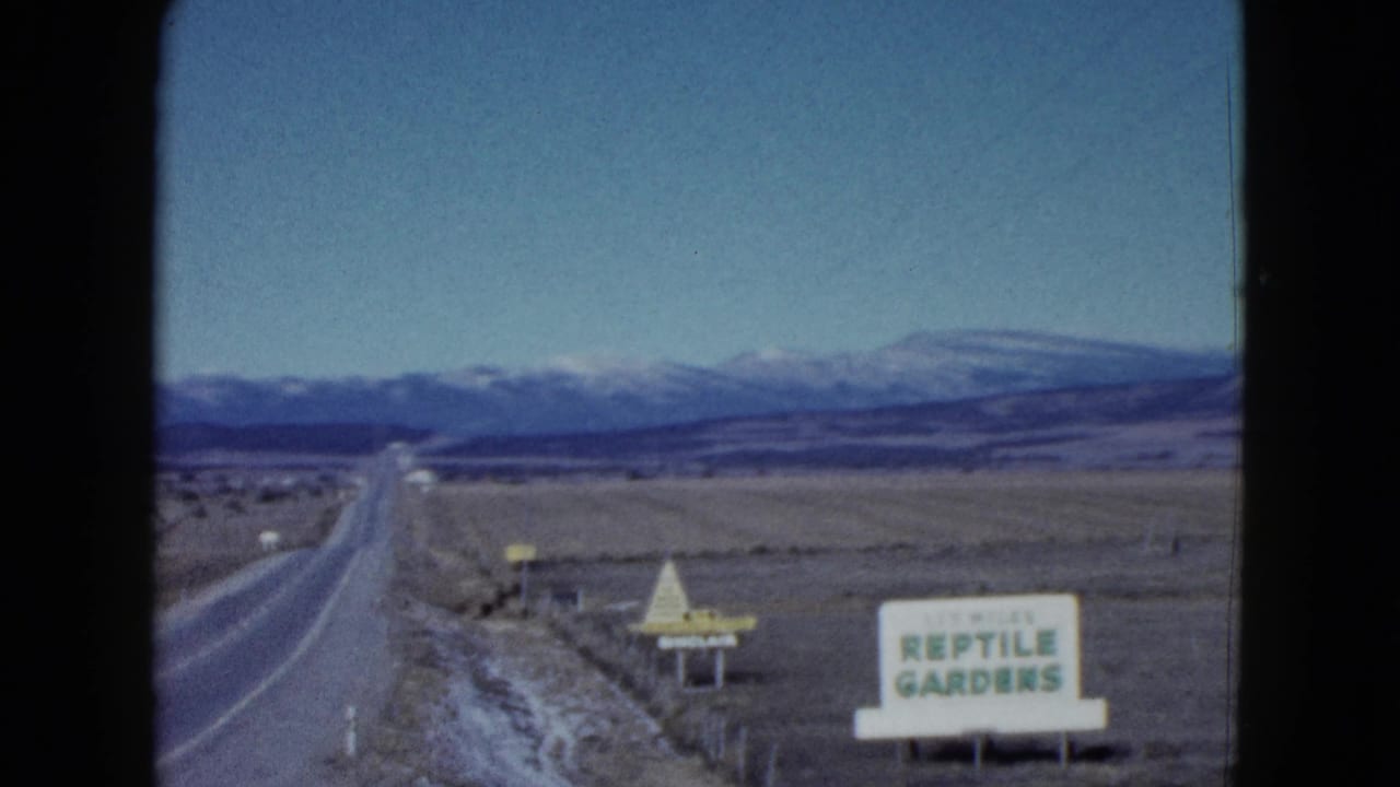 Two-lane highway passing a Reptile Gardens sign with mountains in the distance.