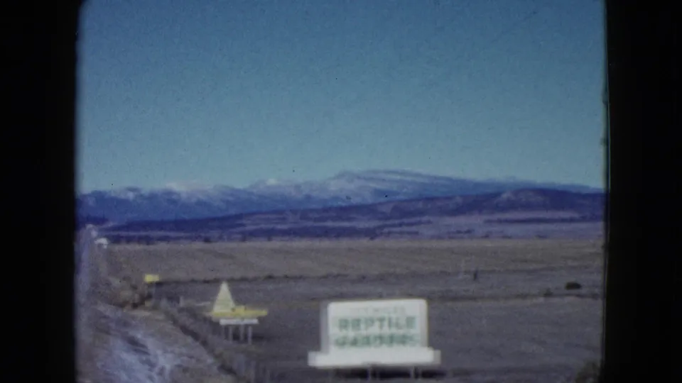 1958 Las Vegas-area roadside scene with the Reptile Gardens sign near the highway and mountains across the horizon.