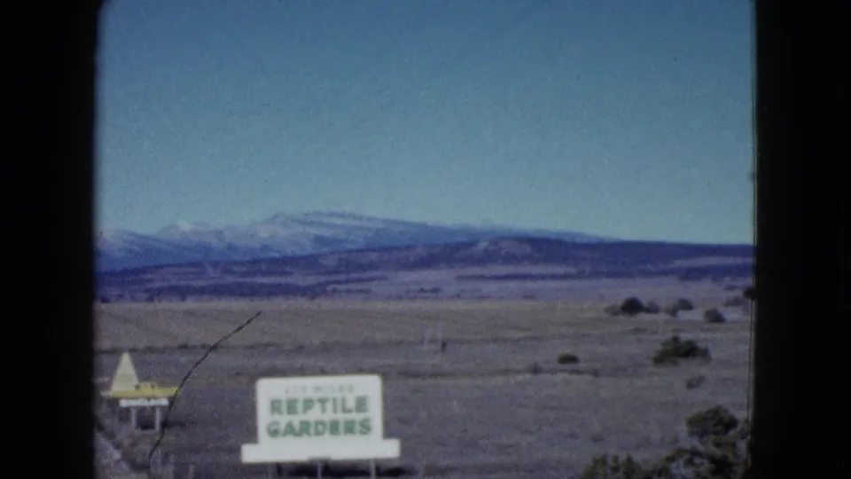 Moving 8mm view near Las Vegas in 1958, showing the Reptile Gardens sign, sparse roadside land, and snow-streaked mountains.