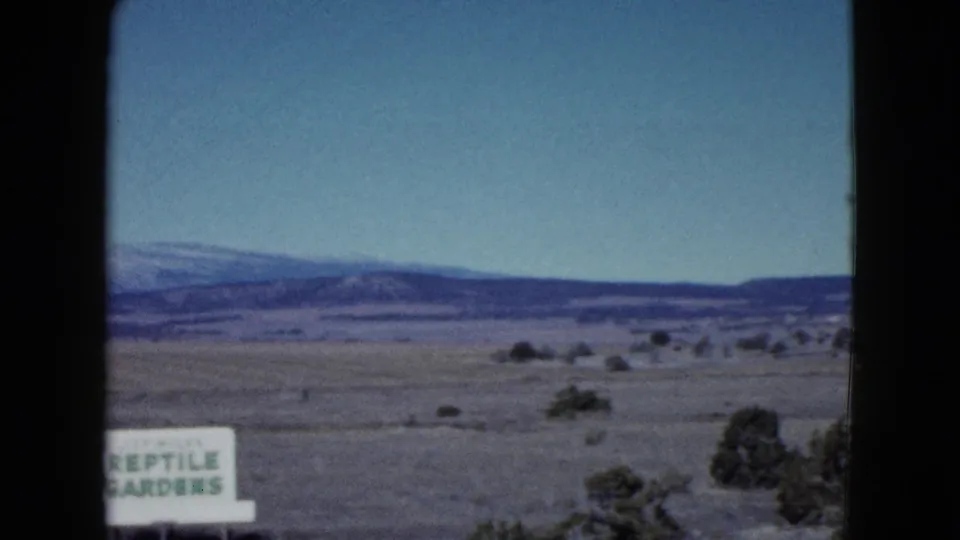 End of the 1958 Las Vegas-area roadside pass, with a partial Reptile Gardens sign, shrubs, open plain, and mountains.