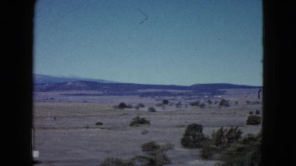 1958 Las Vegas-area desert view from a vehicle, with low shrubs across flat ground and distant hills under blue sky.