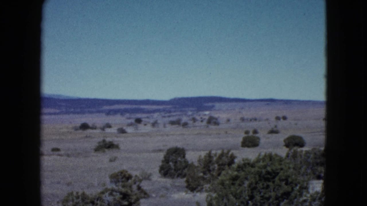 Open desert landscape with shrubs, distant mountains, blue sky, and window framing.