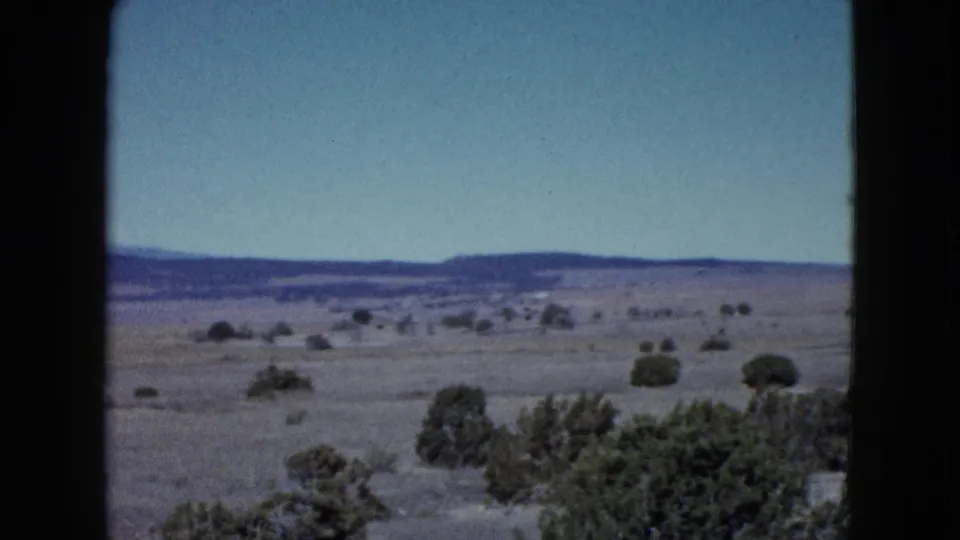 Las Vegas-area 1958 home-movie frame showing open desert, scattered bushes, and low mountains seen through a car window.