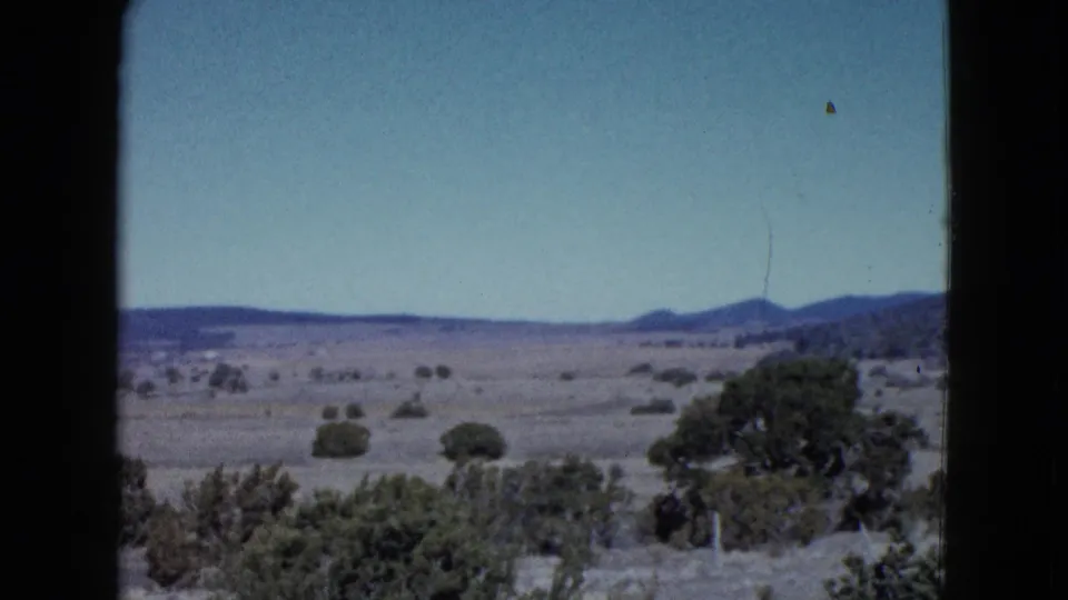 Late-1950s Las Vegas-area desert view with bushes near the camera, open scrubland, and low mountains beyond.