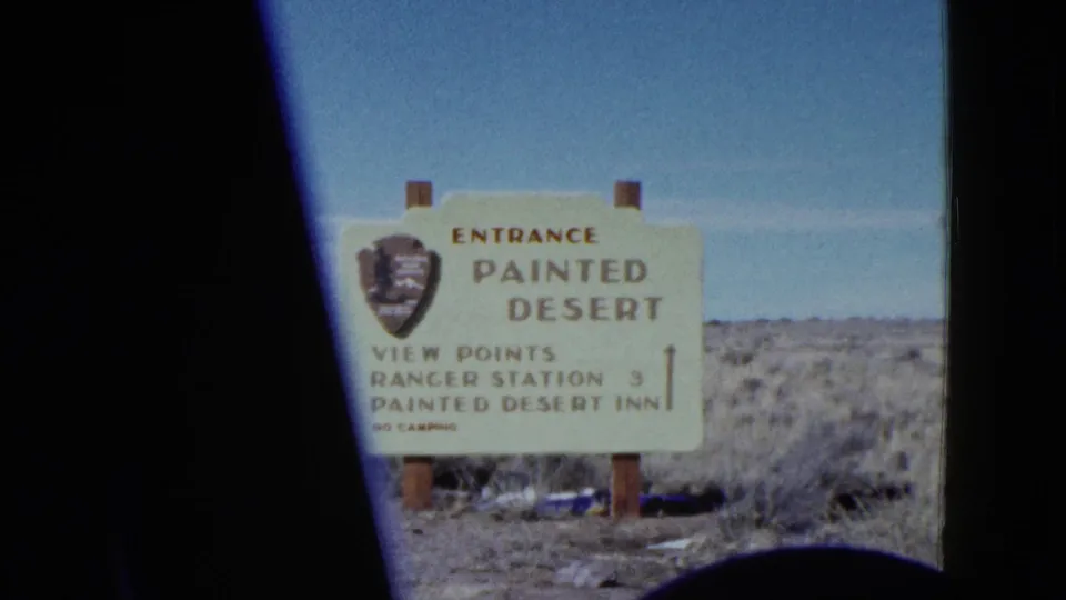 Archival 8mm view of the Painted Desert entrance sign standing on wooden posts amid dry scrubland.