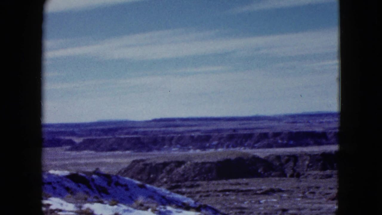 1958 8mm home-movie view of arid desert ridges and flats under a blue sky, likely part of the Painted Desert travel sequence.