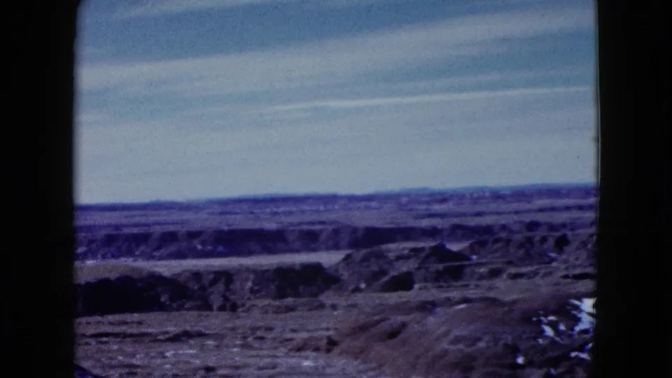 The handheld 1958 travel footage continues across low desert ridges, sparse ground, and a wide blue sky with visible film-frame edges.