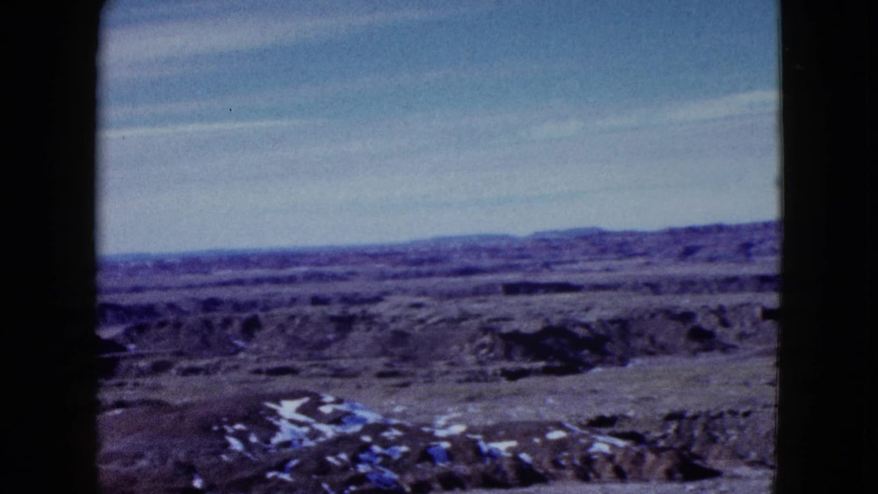 Barren desert landscape with distant mountains, eroded ridges, and light patches in the foreground.