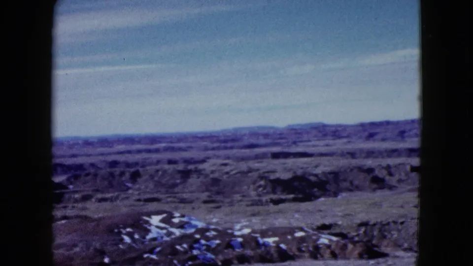 1958 Las Vegas-area frame looking across open desert ridges toward distant mountains, with bright patches on the ground.