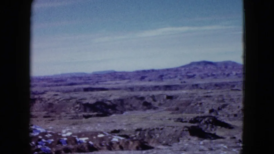 1958 Las Vegas-area home-movie view of dry rocky desert terrain and low hills under a washed pale sky.