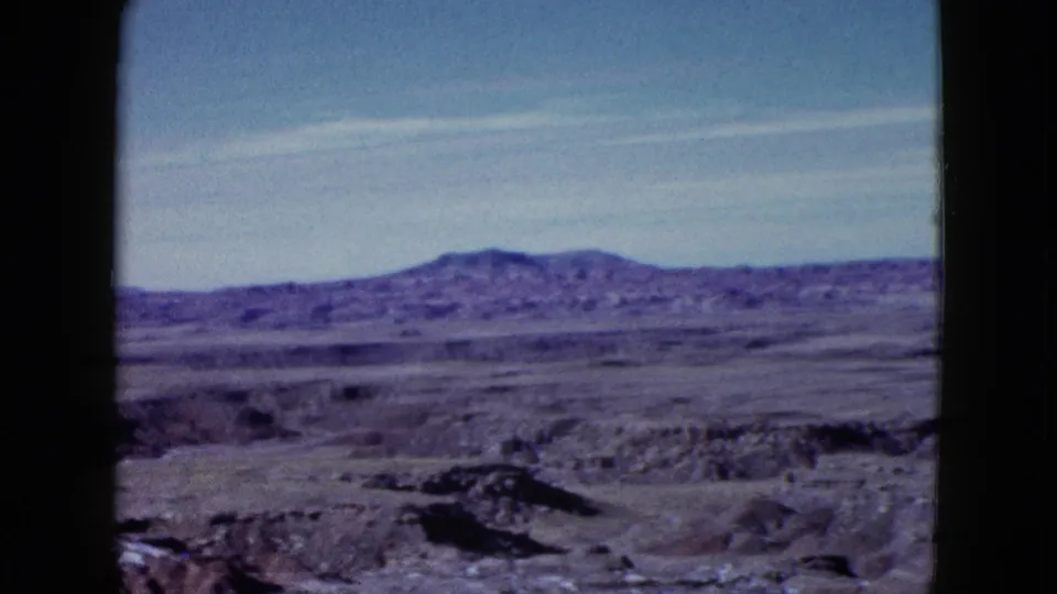 1958 Las Vegas-area frame showing barren ridged terrain and distant mountains during a slow home-movie pan.