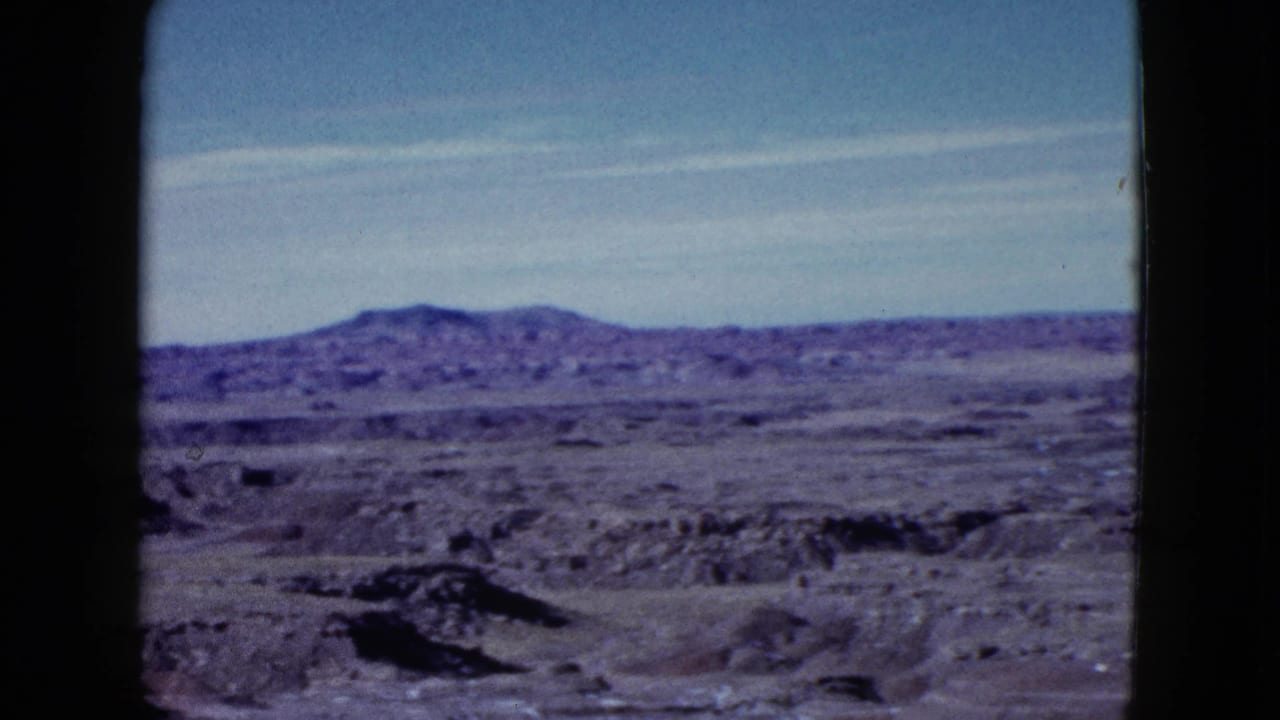 1958 8mm home-movie view near Las Vegas showing rocky desert terrain, distant hills, pale sky, and dark frame edges.