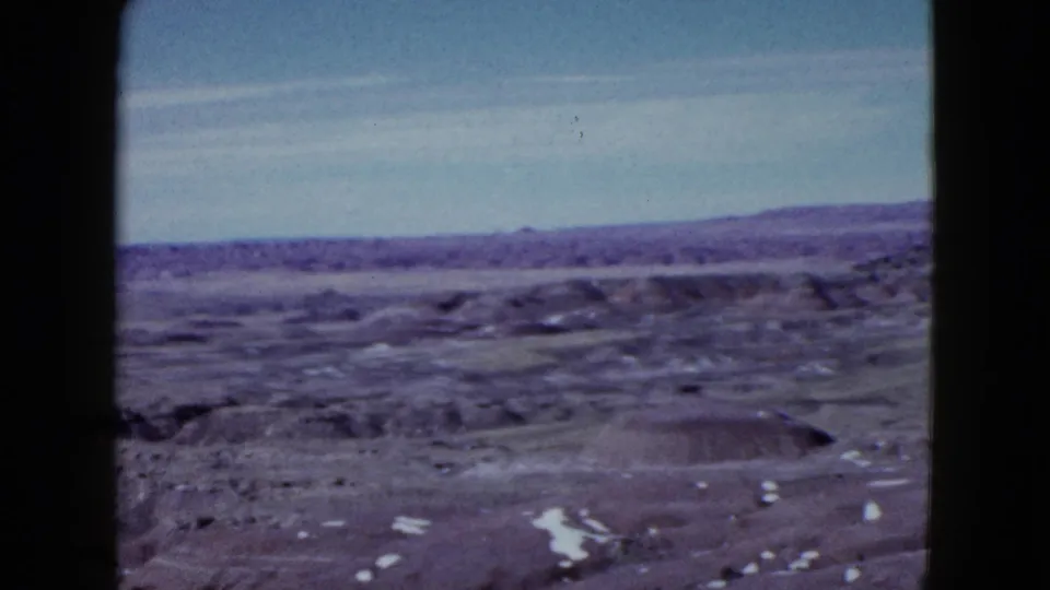 Vintage 8mm view of Las Vegas-area arid terrain with low hills, rough ground, pale sky, and bright white patches possibly snow or salt.