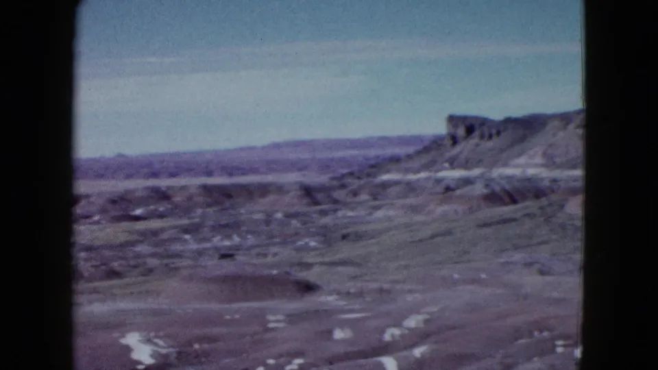 1958 8mm Las Vegas-area landscape showing open desert, scattered white patches, and a mesa-like rocky ridge on the right.