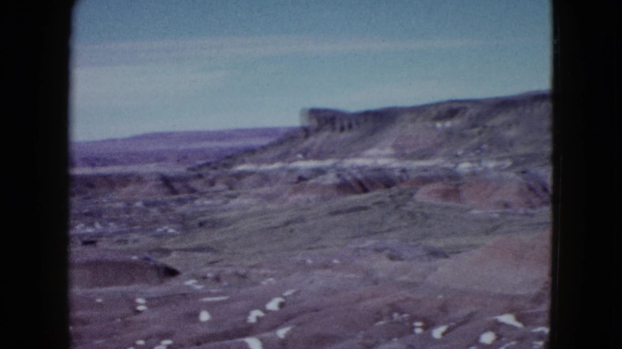 Wide desert view with flat-topped mesa, eroded hills, and pale sky.