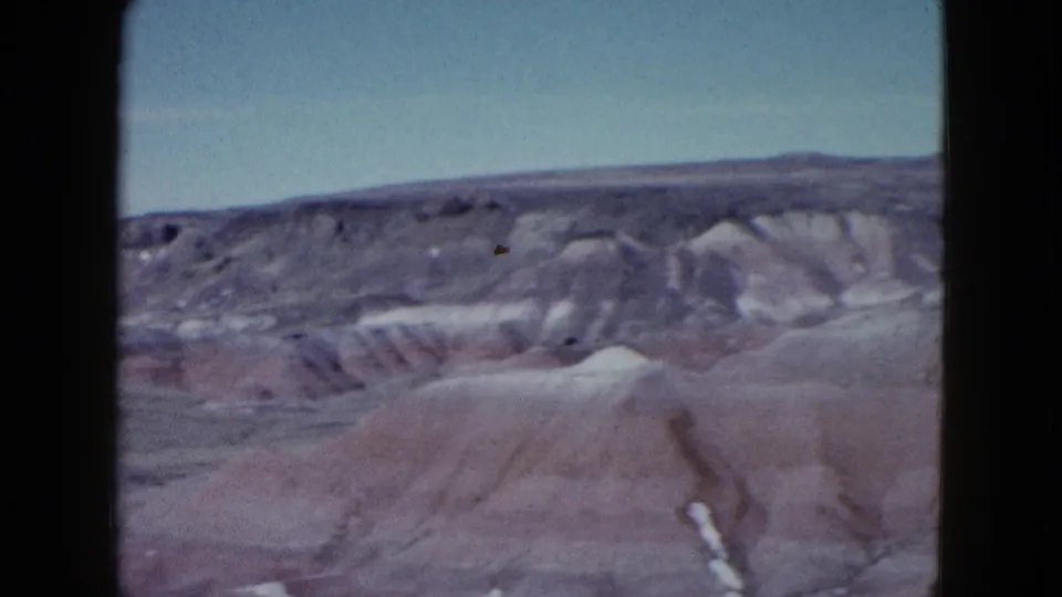 1958 8mm frame showing rounded desert hills, a rocky ridge, and washed-out color from an amateur travel pan near Las Vegas.