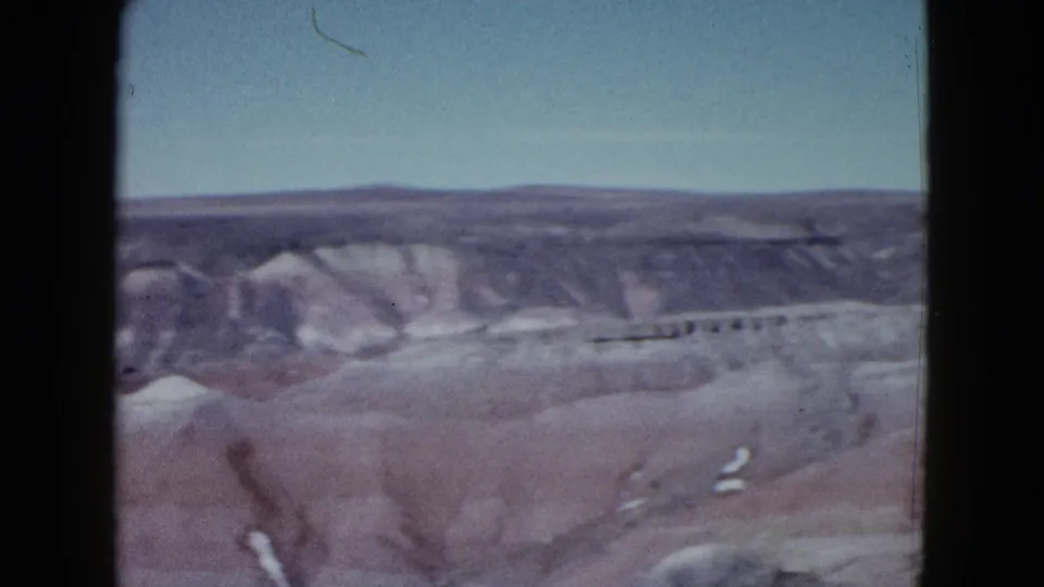 1958 8mm frame near the end of the pan, showing desert gullies, low hills, and a distant ridge in the Las Vegas area.