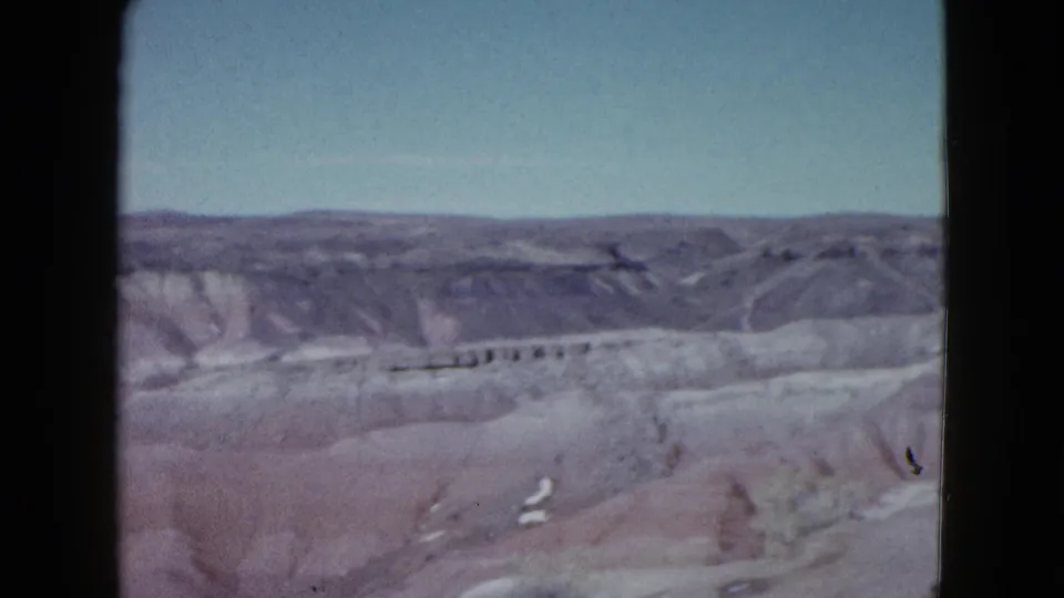 1958 Las Vegas-area 8mm frame showing pale desert terrain, distant ridges, and open sky from a roadside viewpoint.