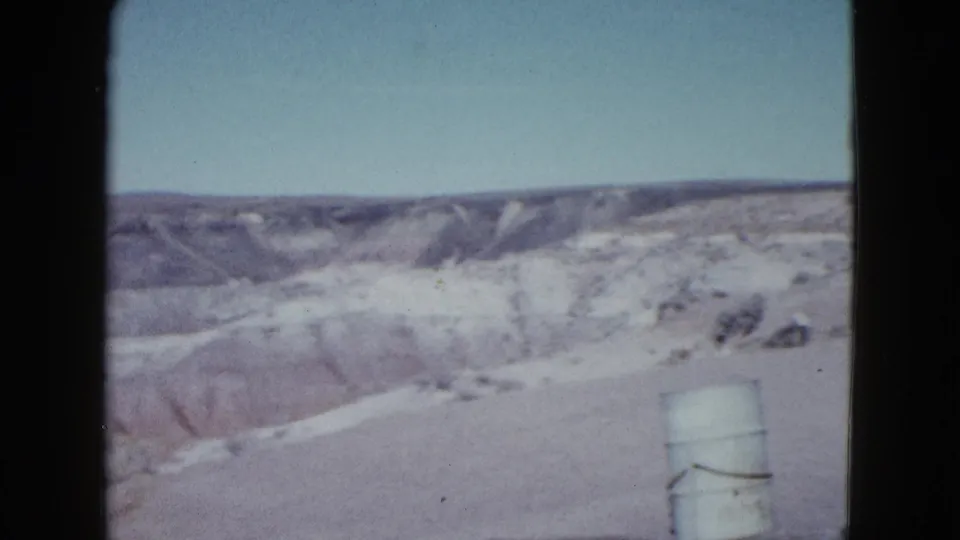1958 Las Vegas-area desert overlook with washed color, distant rock layers, and a roadside barrel near the foreground.