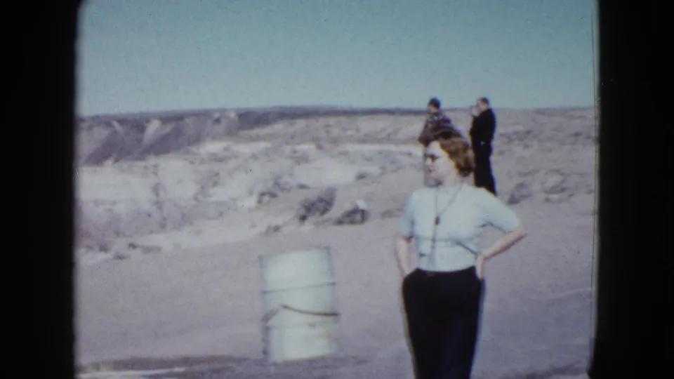 1958 Las Vegas-area home-movie frame showing a woman at a desert overlook, with two adult men behind her and layered hills beyond.