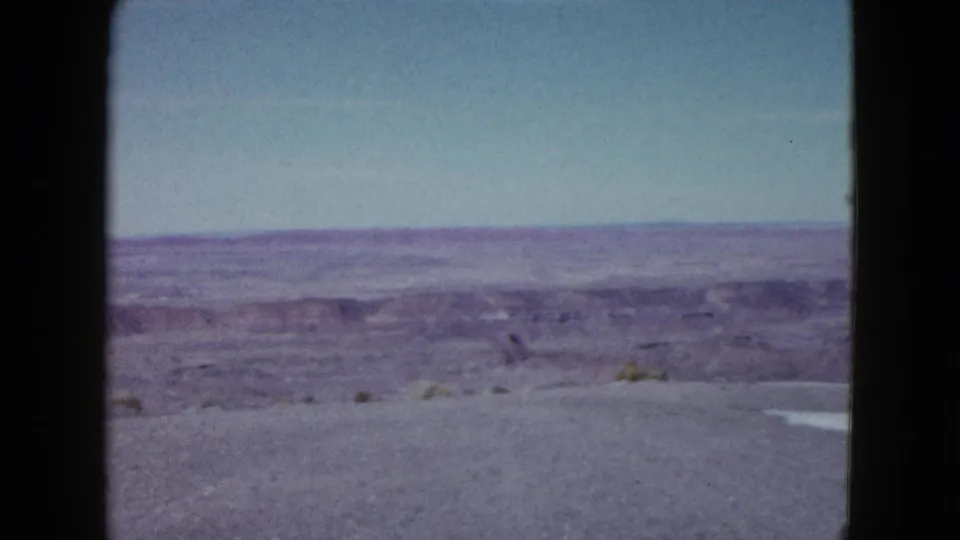 Faded 1958 Las Vegas-area home-movie frame with desert horizon, low brush, gravelly foreground, and soft blue sky.