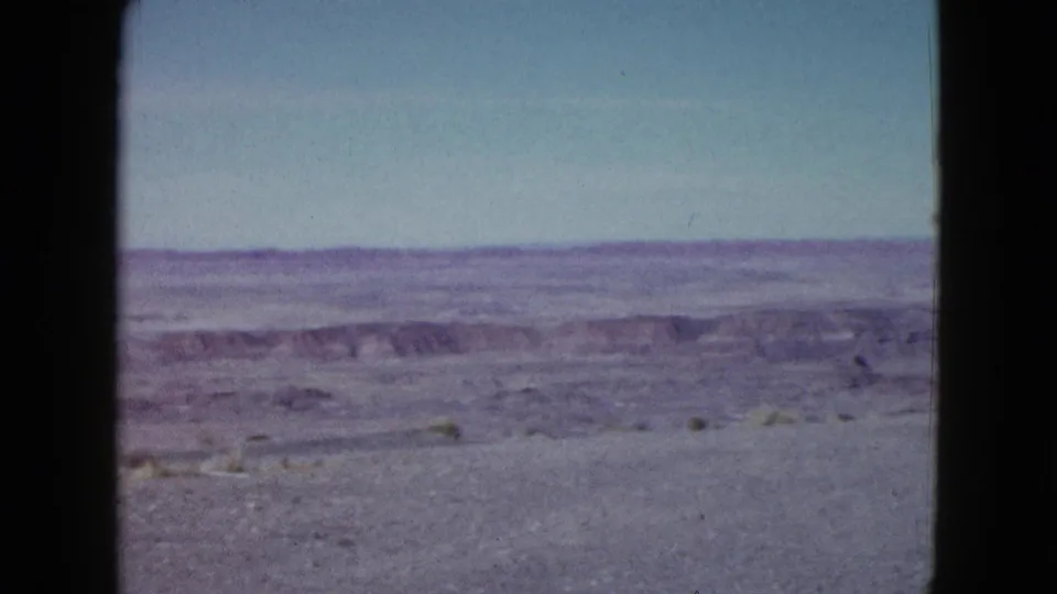 1958 Las Vegas-area 8mm frame showing a distant desert plateau, low ridges, open sky, and sparse foreground brush.