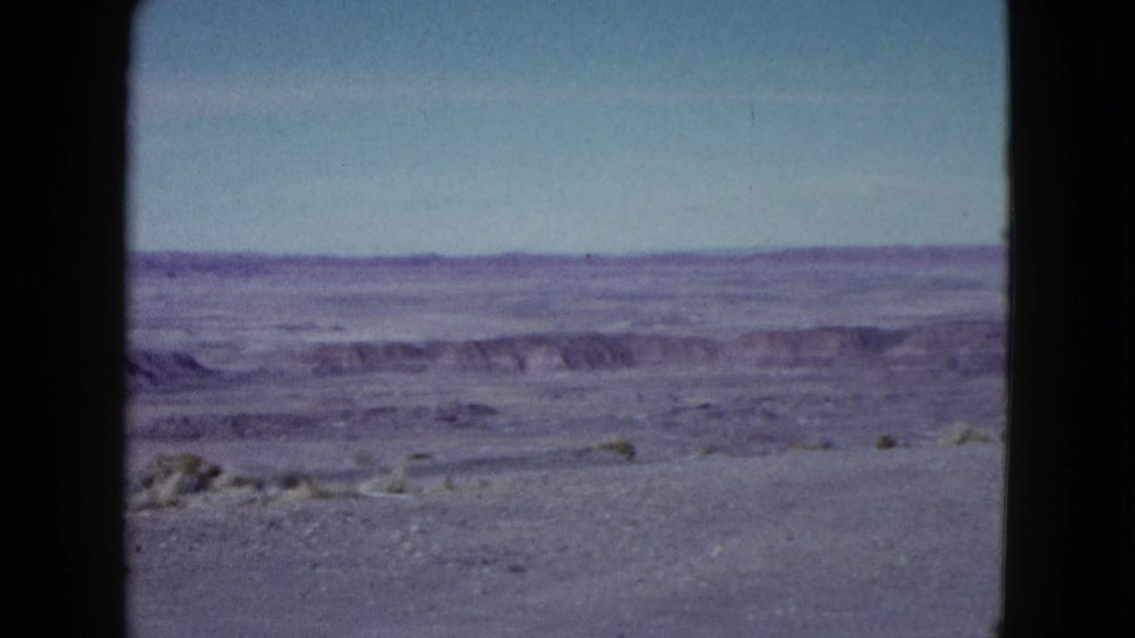 1958 Las Vegas-area 8mm frame showing open desert, low distant ridges, sparse scrub, and dark film borders.