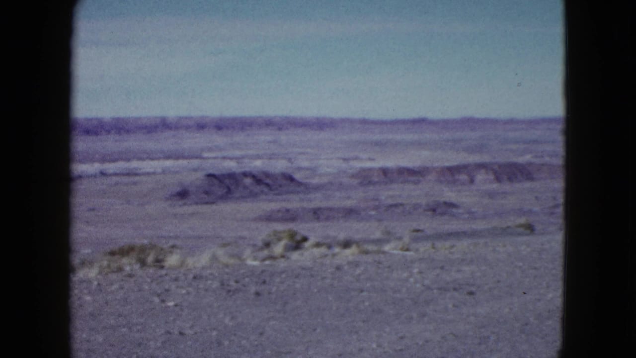 1958 Las Vegas-area 8mm frame with flat sandy desert, low rock formations, sparse vegetation, and faded color.