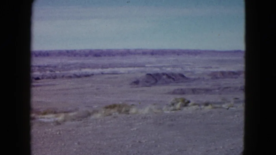 1958 Las Vegas-area 8mm view across scrubby desert foreground toward low horizontal ridges beneath a pale sky.