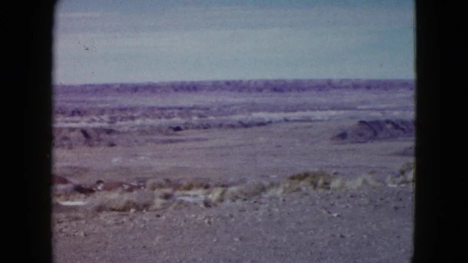 1958 Las Vegas-area 8mm frame showing a wide desert basin, scattered brush, distant low ridges, and purple-toned film color.