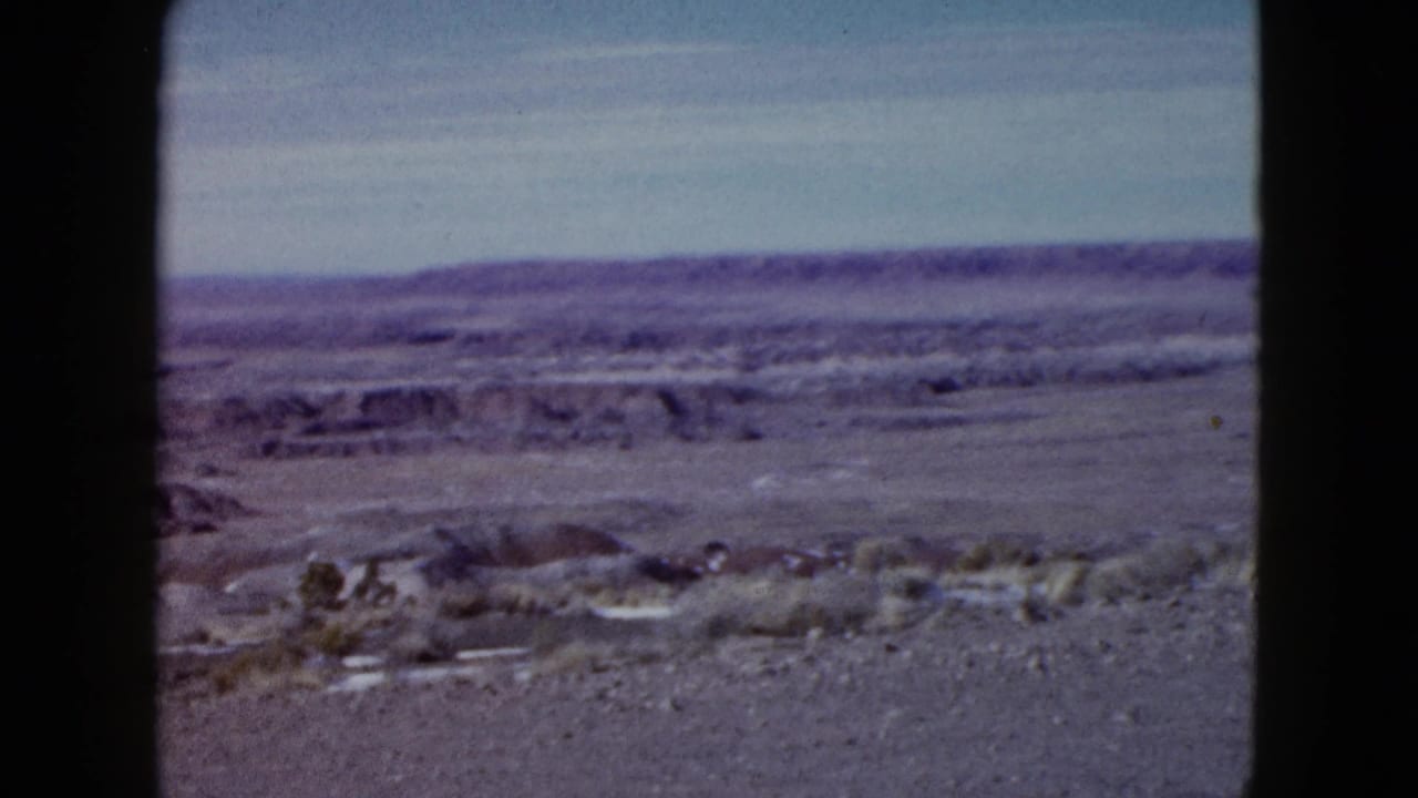 Open arid landscape with scrub, low hills, and a dark center frame divider.