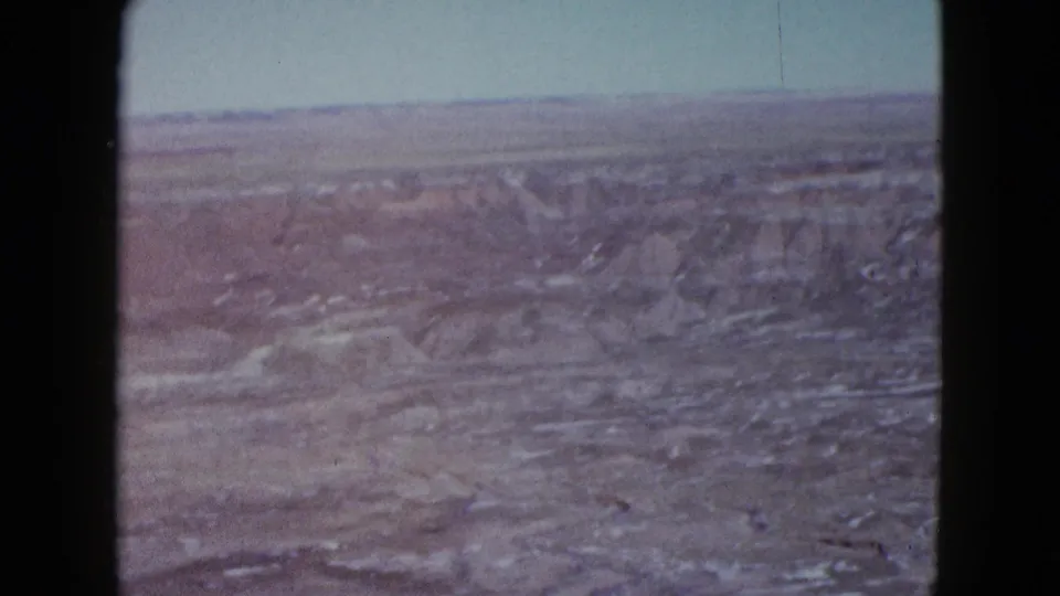 1958 Las Vegas-area home-movie view of eroded desert formations, dry washes, and a flat horizon beneath a pale sky.