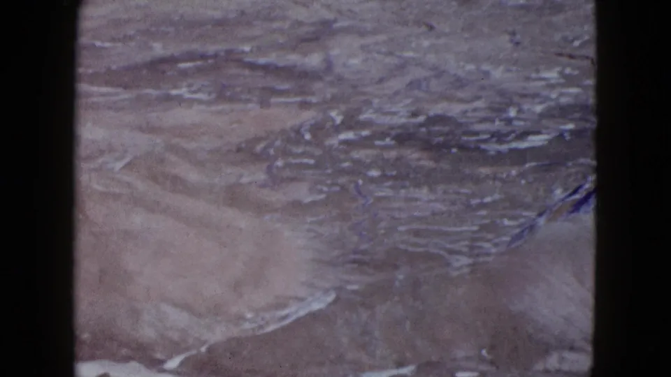 1958 8mm aerial view over rugged desert terrain with layered ridges, dry washes, and muted film color.