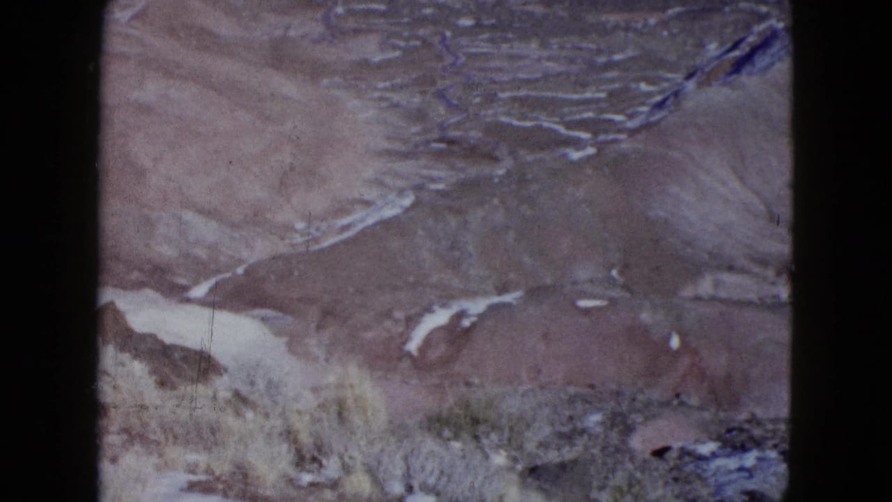 Aerial 8mm view of arid desert hills with pale winding washes and scrub-textured ground, consistent with the clip's 1958 travel footage.