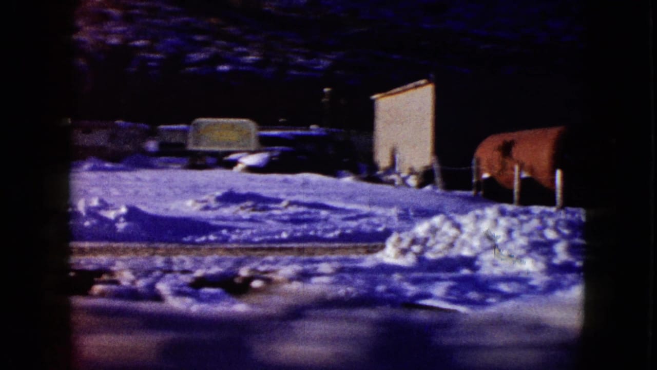Snow-covered roadside with trailers and dark trees seen from a moving car.