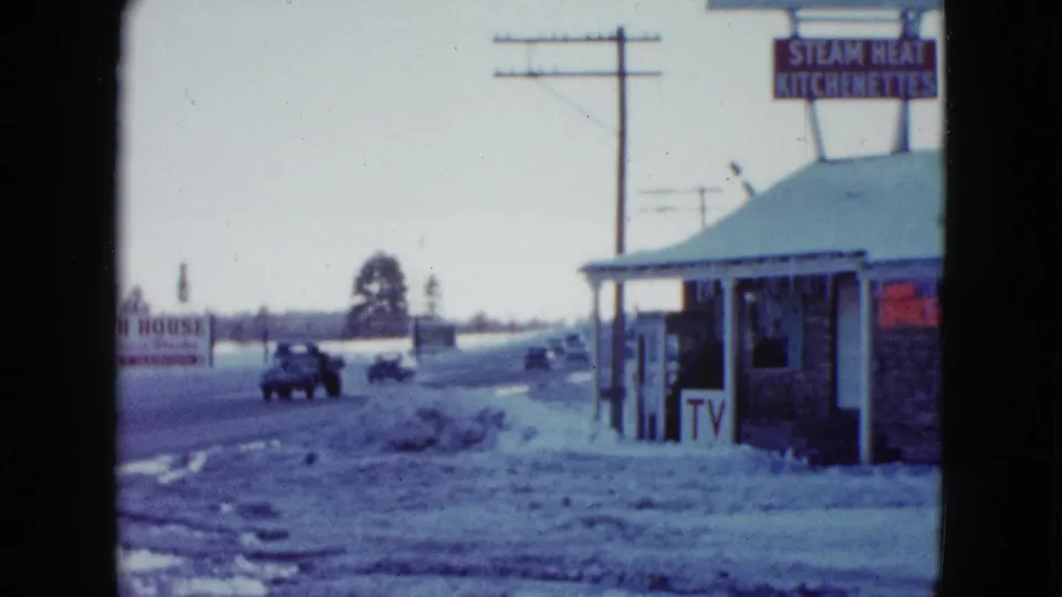 1958 Las Vegas-area roadside building with a Steam Heat Kitchenettes sign, passing cars, snowbanks, and utility poles.