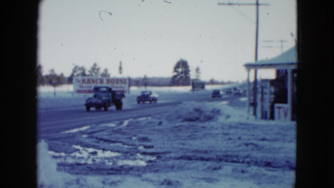 Highway traffic passes a Ranch House sign on a snowy roadside.