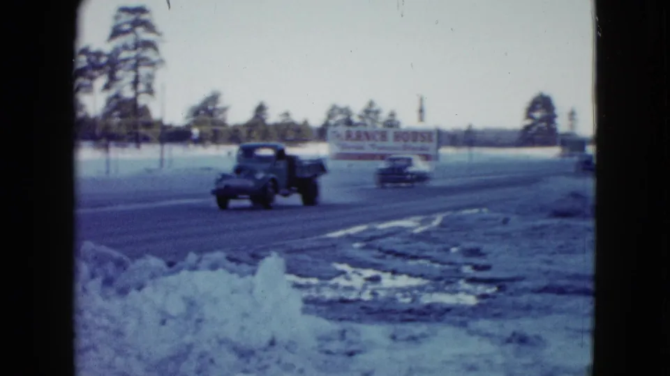 A mid-century truck passes in the foreground on a snowy Las Vegas roadside, with cars, trees, and the Ranch House sign in the background.